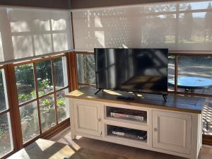 a flat screen tv sitting on a cabinet in a room with windows at Blueberry Hill Vineyard Stay in Rothbury