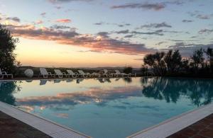 a large swimming pool with chairs and a sunset at Garbo Home in Asciano