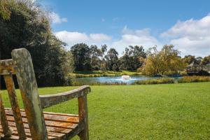 una panchina di legno seduta sull'erba vicino a un laghetto di Briars Country Lodge a Bowral