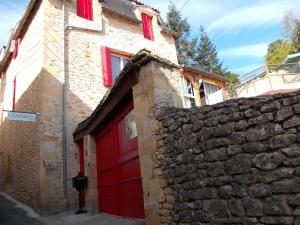 a stone building with a red door and a stone wall at Au Soleil Levant Homestay in Sarlat-la-Canéda