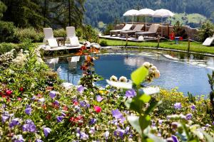 einen Garten mit einem Teich mit Stühlen und Blumen in der Unterkunft GRÜNER Alpengasthof inkl Summercard in Sölden