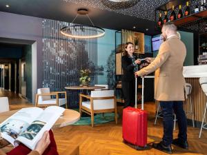 Un uomo e una donna con una valigia rossa in un ristorante di Mercure Saint Omer Centre Gare a Saint-Omer