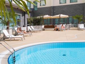 two people sitting in chairs next to a swimming pool at Novotel Milano Malpensa Aeroporto in Cardano al Campo