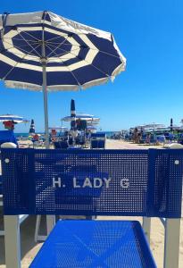 a blue bench with an umbrella on the beach at Hotel Lady G in Tortoreto Lido