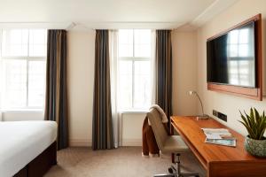 a bedroom with a bed, desk, chair and window at The Clermont London, Charing Cross in London