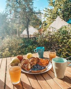 a plate of food on a wooden table with drinks at Dragonfly Gardens Urban Glamping Brasov in Braşov
