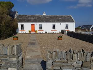 ein weißes Haus mit einer orangefarbenen Tür und einem Steinzaun in der Unterkunft The Coral Cottage in Doolin