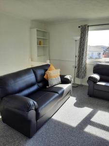 un sofá de cuero negro en una sala de estar con ventana en 2 Storey 3 Bedroom Chalet -Outdoor Swimming Pool - sleeps up to 6 - 5 min walk to the Beach, near Broads and Great Yarmouth en Scratby