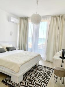 a white bedroom with a bed and a large window at Vila Adriano pe plaja Belona in Eforie Nord