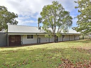 une maison blanche avec un arbre dans la cour dans l'établissement Malolo Park Guest House, à Quorrobolong