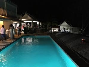 - une piscine bleue la nuit avec des personnes debout dans l'établissement Coco Beach Marie-Galante, à Grand-Bourg