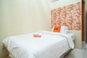 a white bed with an orange pillow on top of it at KoolKost Syariah at Ir Soekarno Solo Baru in Solo