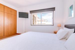 a white bedroom with a large bed and a window at AL- Apartamentos Novos Vista Mar in Quarteira