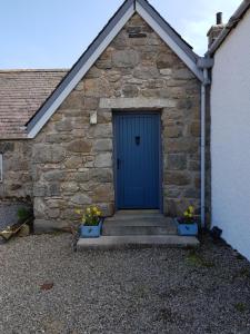 a blue door on a stone building with flowers at Jakels Rest in Lairg