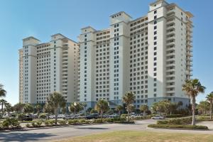 a large white building with palm trees in a parking lot at The Beach Club Resort and Spa in Gulf Shores