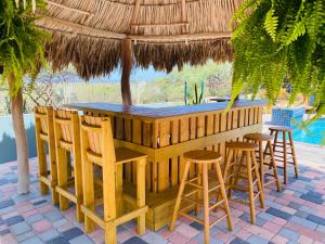 una barra de madera con taburetes bajo una sombrilla de paja en La Felicidad Aruba, en Oranjestad