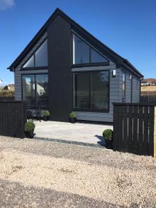 uma casa preta com janelas grandes e uma cerca em Braeside Bothy em Dunvegan