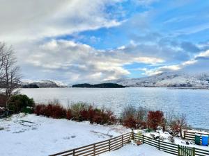 a snowy lake with a fence and snow covered mountains at Loch Morar Private Suite in Mallaig
