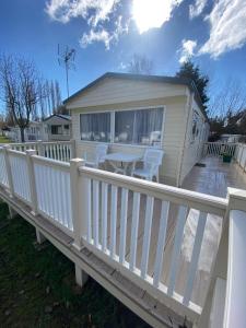a house with a white fence and a table on a deck at KellysHolidayHomes Atlas 3 bedrooms caravan in Weeley