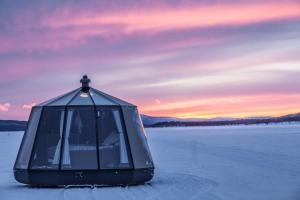 un igloo di vetro su un lago ghiacciato con un tramonto di Laponia Sky Hut a Gällivare