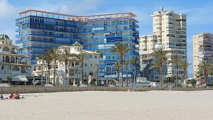 a group of people sitting on the beach in front of buildings at Exclusif Appartement en 1er Ligne, Vue Imprenable, Piscine, Parking Privé à Playa Mucha Vista, Alicante in El Campello