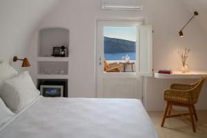 a bedroom with a bed, chair and a window at Canvas Suites in Oia