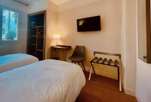 a bedroom with two beds and a chair and a television at Hotel Courbet in Juan-les-Pins