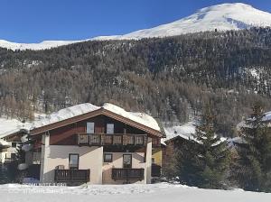 a house in the snow with a snow covered mountain at Baita Stella Alpina in Livigno