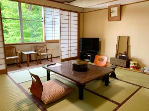 a living room with a table and chairs and a tv at Kirishimaya Ryokan in Kusatsu