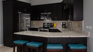 a kitchen with black cabinets and blue bar stools at A Wave From It All @ Aqueducts in Negril