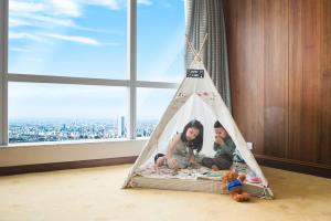 twee kinderen in een tipi tent in een kamer met een raam bij InterContinental Hanoi Landmark72, an IHG Hotel in Hanoi