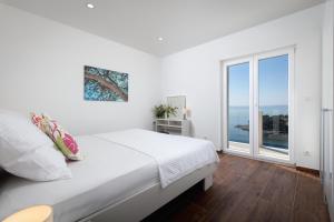 a white bedroom with a bed and a large window at APARTMENTS BAKA in Selca