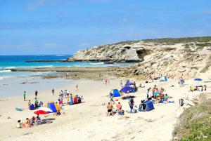 um grupo de pessoas em uma praia com guarda-sóis em Die Waenhuis em Arniston