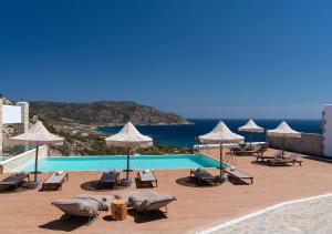 una piscina con sedie, ombrelloni e oceano di SOPHID Wellness Suites Karpathos a Karpathos