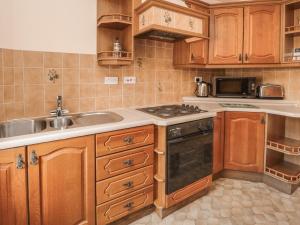 a kitchen with wooden cabinets and a sink and a stove at Manor Cottage in Wooler