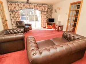 a living room with a leather couch and a television at Fern Cottage in Wooler