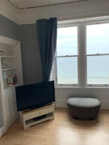 a living room with a flat screen tv and two windows at Bass Rock Beachside Flat in North Berwick
