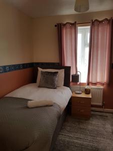 a bedroom with a bed and a window with pink curtains at Delight Marvel-Derby House at Maidstone in Maidstone