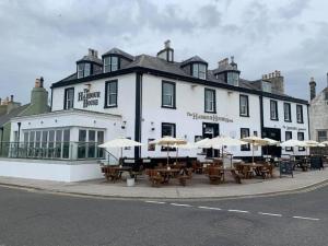 un grand bâtiment blanc avec des tables et des parasols dans l'établissement The Harbour House Sea front Hotel, à Portpatrick