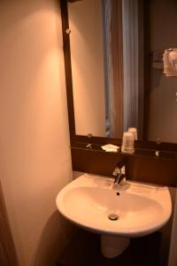 ein Badezimmer mit einem weißen Waschbecken und einem Spiegel in der Unterkunft Hôtel de Bourgogne in La Clayette