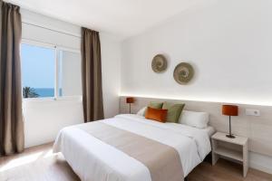 a white bedroom with a large bed and a window at Apartamentos Venecia in Lloret de Mar