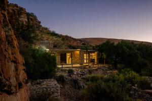 a stone house on a mountain with the lights on at Desert Wind Private Guest and Game Farm in Montagu