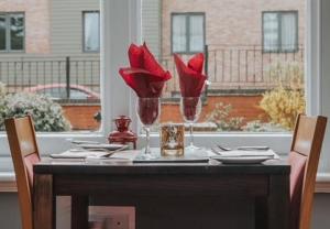 a dining room table with red flowers in glasses at The Quorn Lodge Hotel in Melton Mowbray