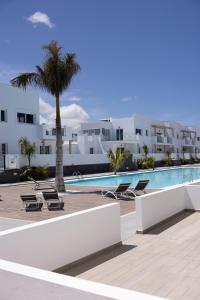 a swimming pool with a palm tree and white buildings at Island Home Fuerteventura in Corralejo