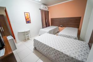 a hotel room with two beds and a television at Hotel Tadini in Santa Rita do Sapucaí