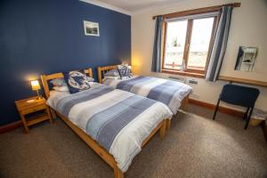 two beds in a room with blue walls and a window at Arle Lodge in Tobermory