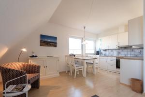 una cucina con mobili bianchi, tavolo e sedie di Haus Nordseegruss, App 4 a Wenningstedt