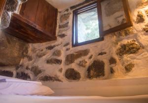a bedroom with a stone wall and a window at Palaiokastro Traditional House in Mandrákion