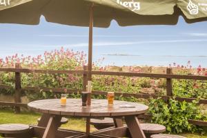 a picnic table with two drinks and an umbrella at The Bamburgh Castle Inn - The Inn Collection Group in Seahouses