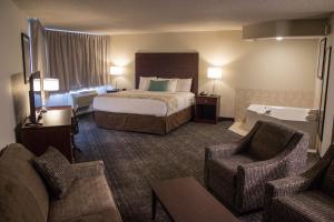 een hotelkamer met een bed en twee stoelen en een bad bij Cobblestone Suites - Oshkosh in Oshkosh